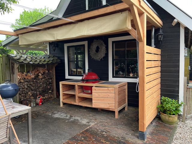 Maatwerk buitenkeuken met kamado-barbecue onder een houten veranda met windscherm