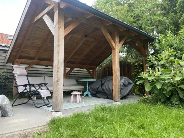 Houten overkapping met pannendak boven een loungehoek in de tuin