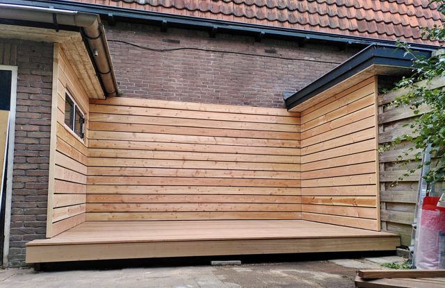 Beschutte terrashoek tegen de gevel met wanden en verhoogde vlonder van lariks