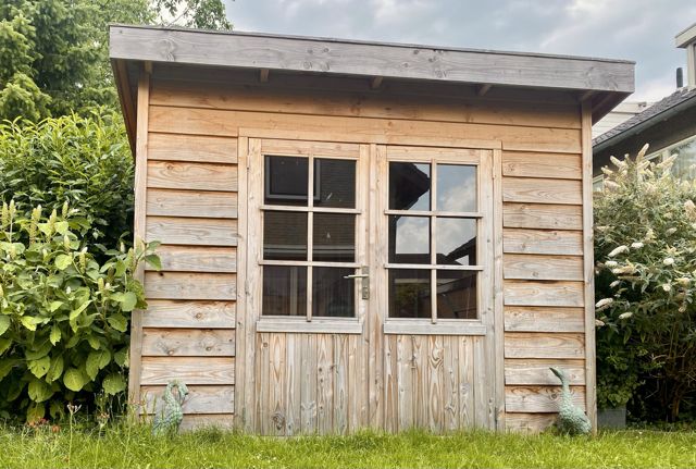 Tuinhuis met plat dak, vergrijsde gevelbekleding en dubbele deuren met glas